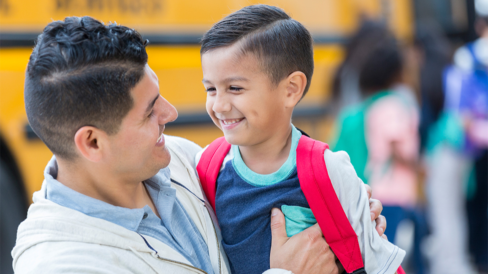 A man and a young boy in front of a school bus