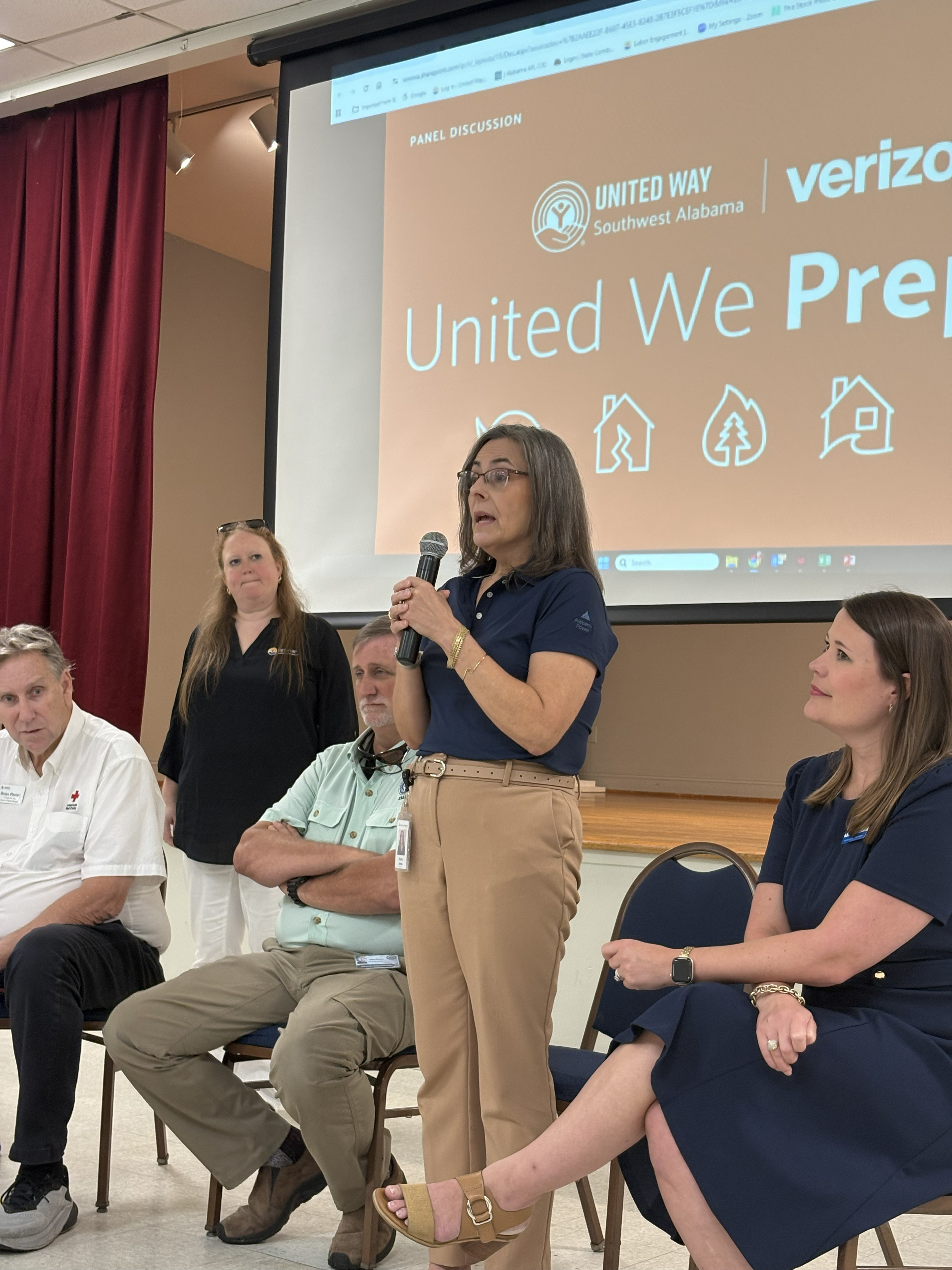 Disaster Workshop Panel. Four presenters - two men and two women, woman from Alabama is standing speaking into the background. Third woman looks on. Screen behind reads United Way & Verizon, United We Prepare