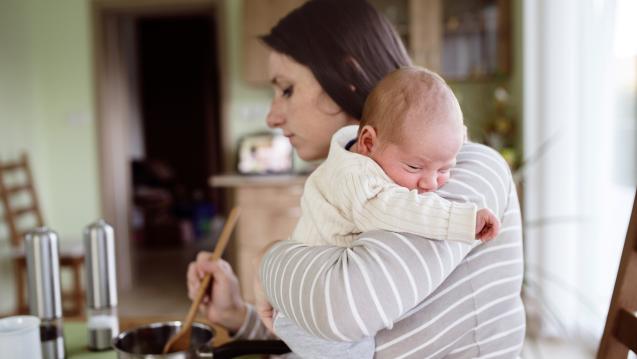 Woman holding a baby while cooking on a stove