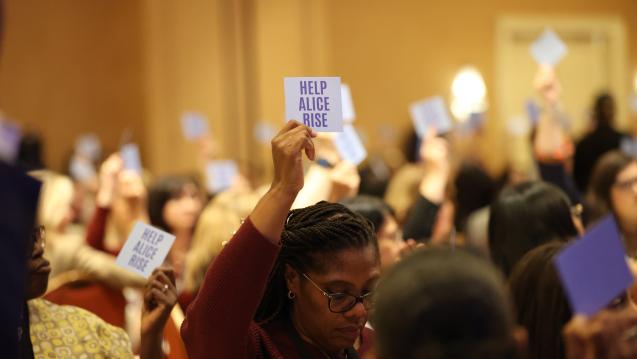 Woman holding a card that says "Help ALICE Rise"