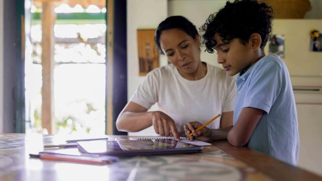 A mother is helping her son with his homework at a table