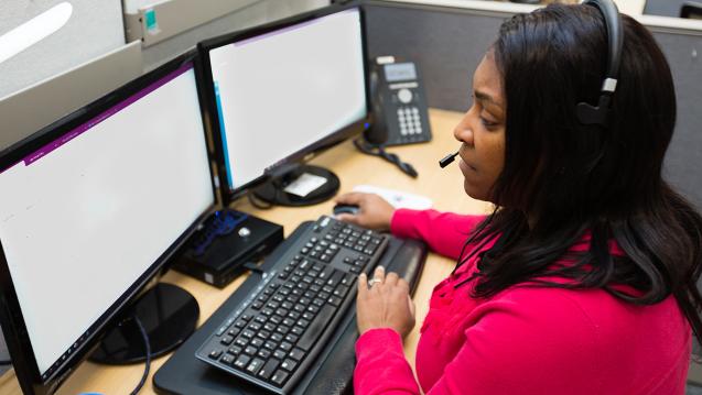 A 211 operator looking at two computer screens while taking call