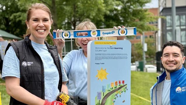 Volunteers from United Way Worldwide and United Way National Capital Area smile holding a level and shovels to install a new Born Learning STEAM Trail in Alexandria, Va.