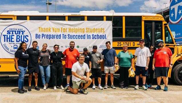 Stuff-the-Bus volunteers with United Way of Greater Nashville pose in front of a school bus at Nissan Stadium