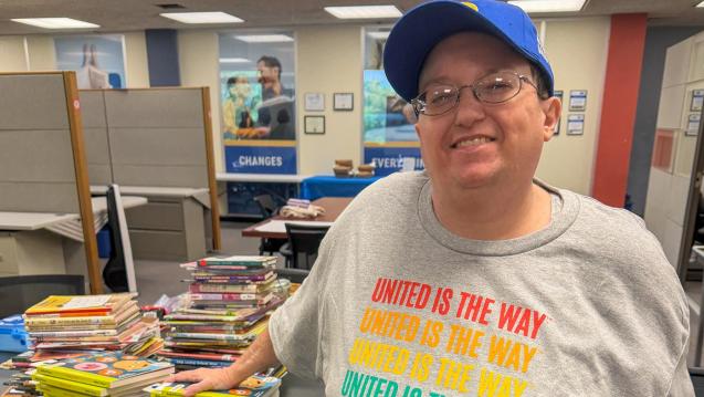 KD Musser, a dedicated volunteer with United Way Rock River Valley in Rockford, IL, stands with her hand on a stack of books
