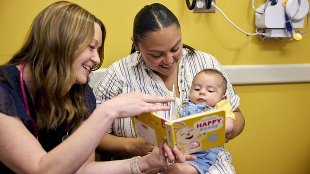 A mother and child read a book with a medical professional in a doctor's office. 
