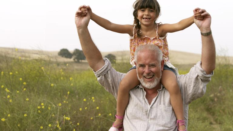 A man is carrying a little girl on his shoulders in a field.
