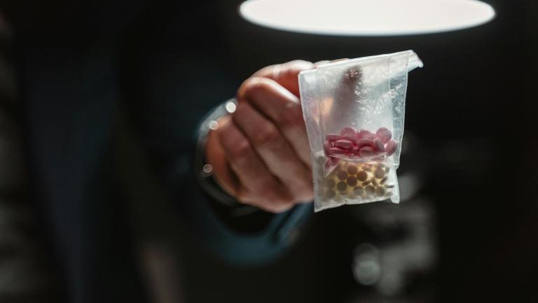 Person holding a small plastic bag of pills and tablets