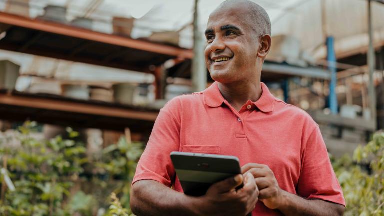 Man in light red shirt holding a tablet at work