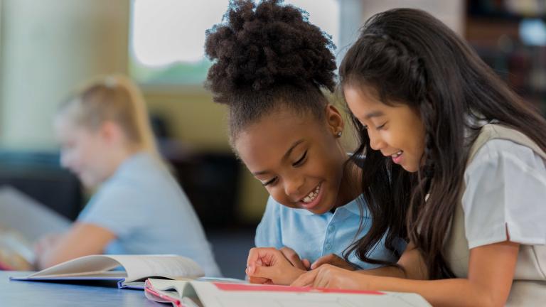 Two young girls reading a book together