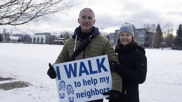 Man and wife holding sign that reads "I walk to help my neighbors"
