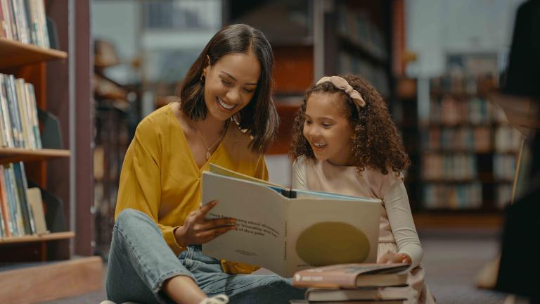 young woman reads a book with a child in a library