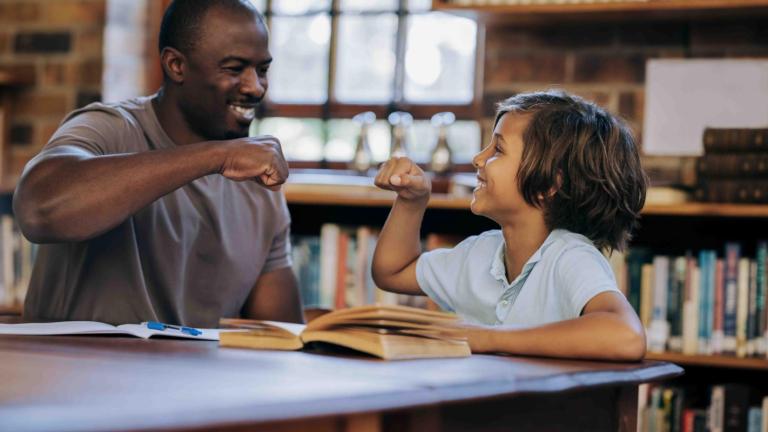 A mentor and child about to fist bump in the library