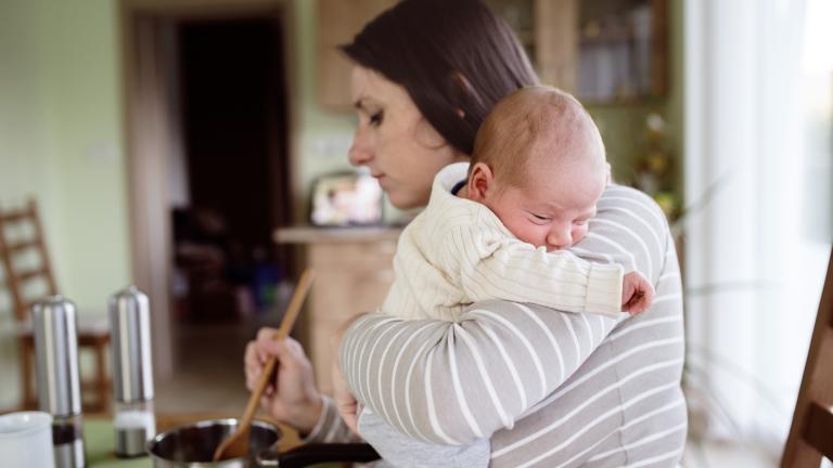 Woman holding a baby while cooking on a stove
