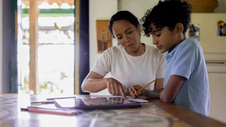 A mother is helping her son with his homework at a table