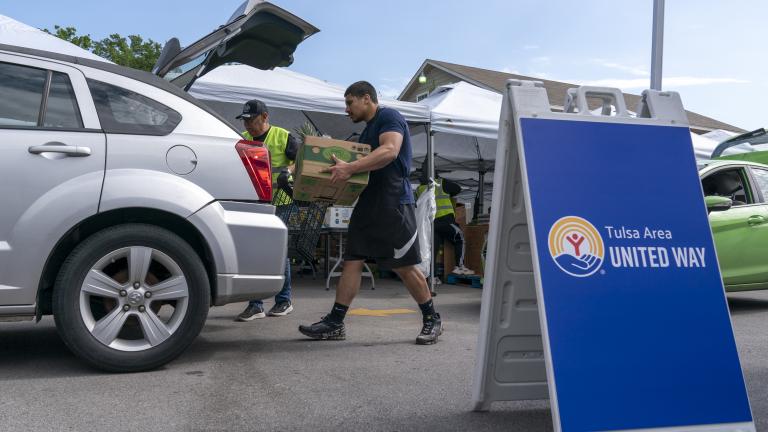 Two men loading food into the trunk of a car at a food distribution site