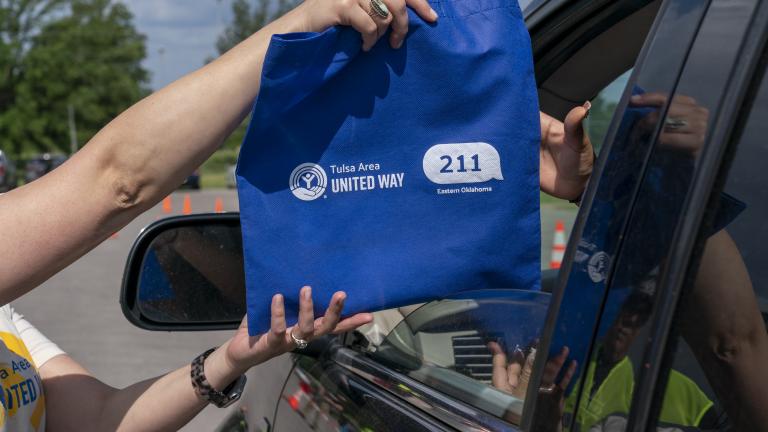 Person handing 211 bag to a driver in a drive through food distribution line