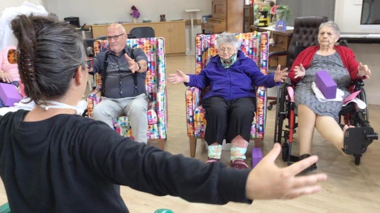 Participants in a chair yoga class open their arms