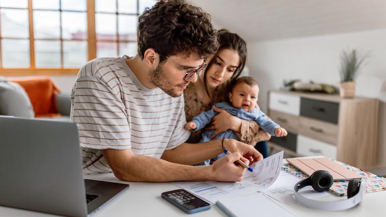 A man huddling over a bill while a woman and baby look over his shoulder 