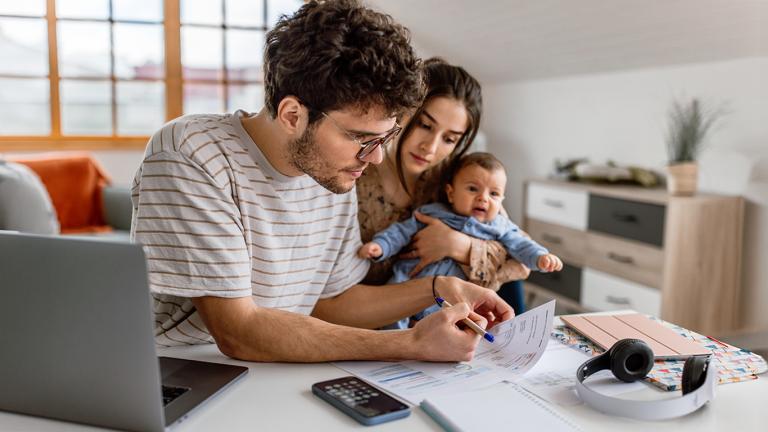 A man huddling over a bill while a woman and baby look over his shoulder 