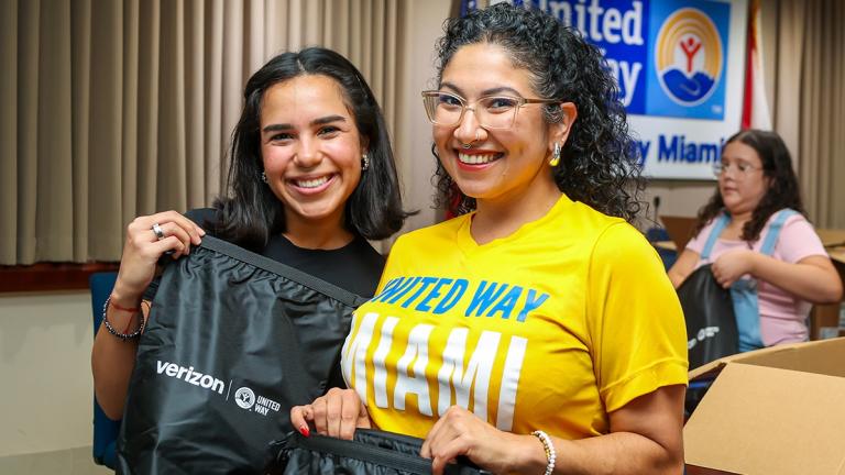 Two United Way of Miami staffers smiling as they hold emergency preparedness kits