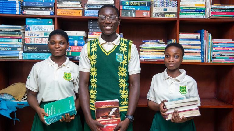 Three students holding books and smiling