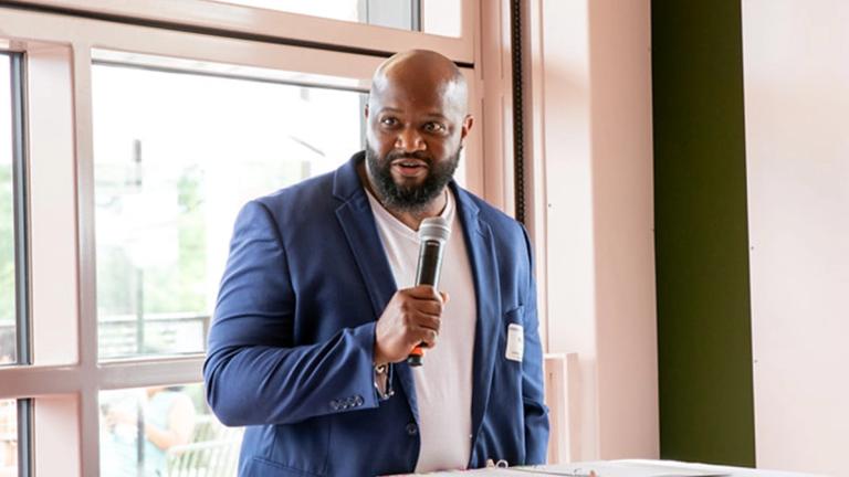 Naphtali Bryant standing at a podium, holding a microphone