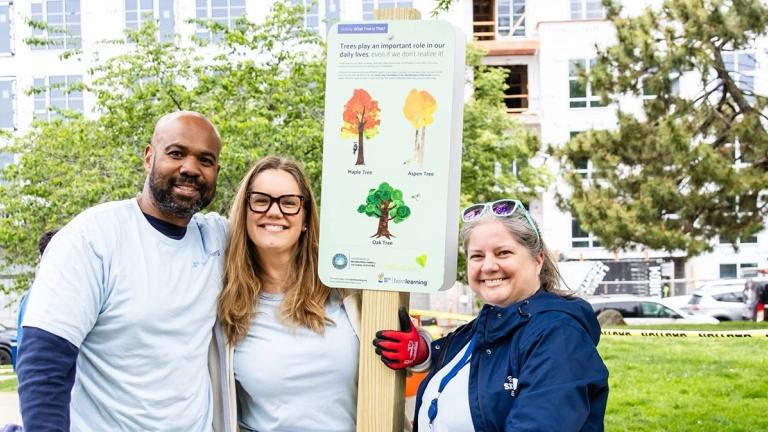 Three United Way volunteers smile by a Born Learning STEAM Trail sign
