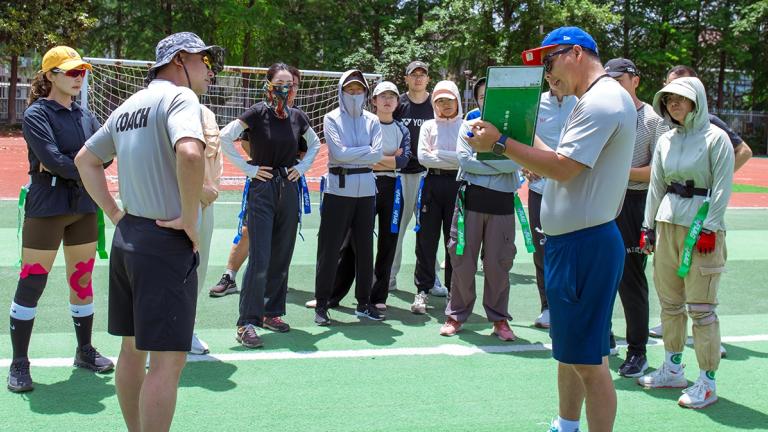 A flag football coach holds a clipboard explaining a play as part of a United Way Worldwide initative to improve youth fitness in China