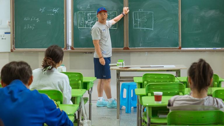 A coach stands at a chalkboard to explain flag football rules and plays to students in China, where United Way and the NFL is working to expand the sport