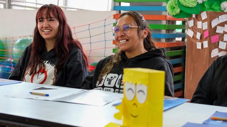 Two women participating in a workshop smiling while seated as a table.