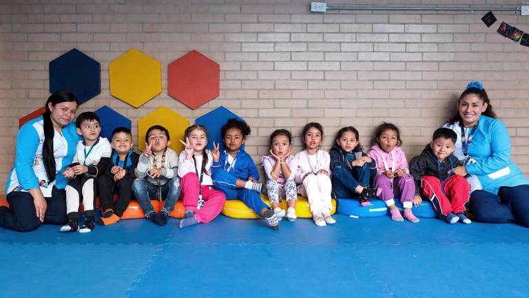 A group photo of preschoolers sitting on the floor against a wall with their teachers at Ojo de Perdiz Preschool, where United Way Colombia supports early childhood education