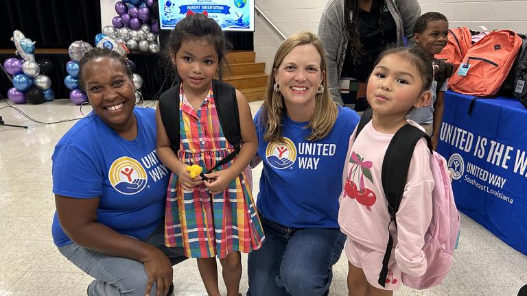 Two United Way of Southeast Louisiana staffers smiling with two little girls who received school supplies through a back-to-school event at the New Orleans Resiliency Center
