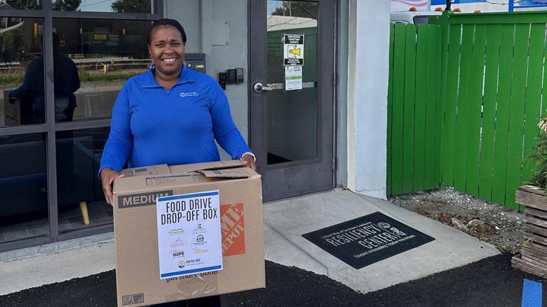 A woman with United Way of Southeast Louisiana holds a box of food donations in front of the New Orleans Resiliency Center