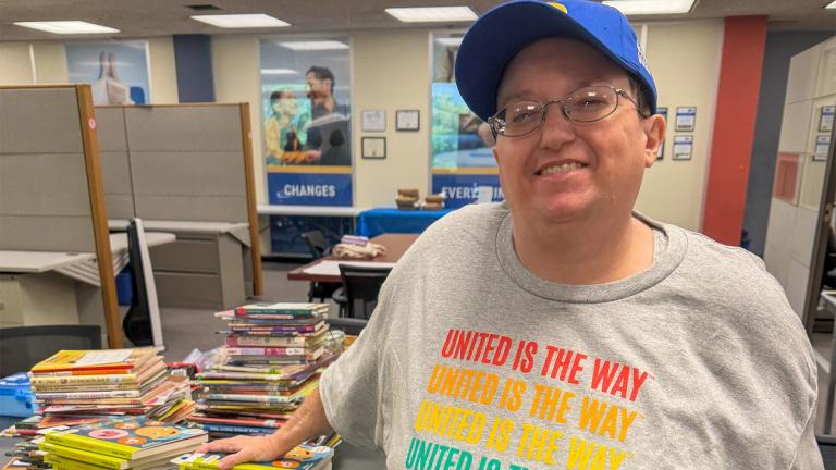 KD Musser, a dedicated volunteer with United Way Rock River Valley in Rockford, IL, stands with her hand on a stack of books