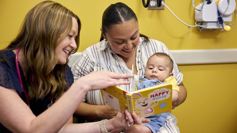 A mother and child read a book with a medical professional in a doctor's office. 