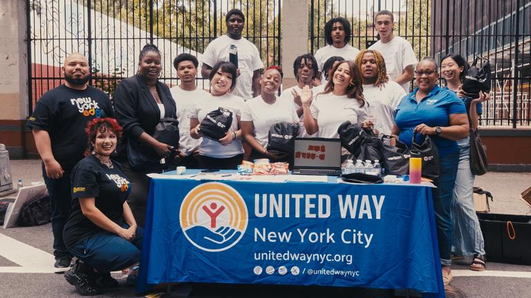 A group photo of the Resiliency Ambassadors behind a table with a banner that reads United Way New York City. 