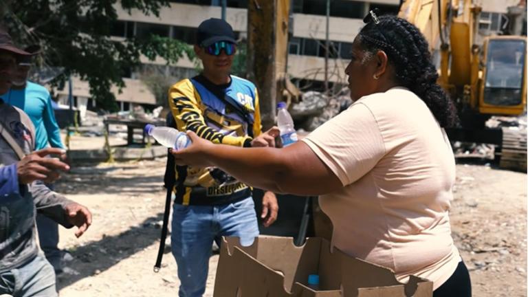 A woman handing water bottles to construction workers as they rebuild damage from earthquakes in Venezuela.  