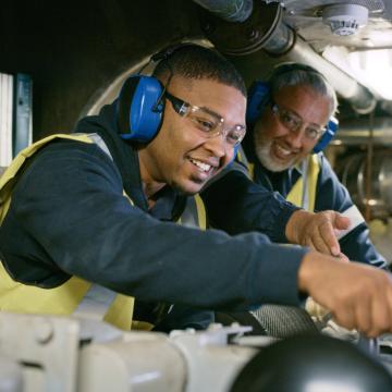 Young worker learning from experienced worker in machine shop