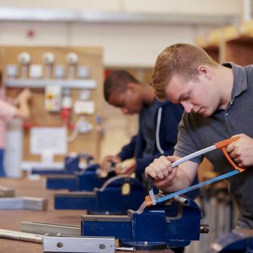 Teenager cutting with a saw in class