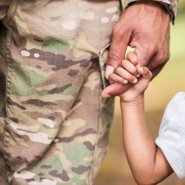 Adult wearing military pants holding child's hand.