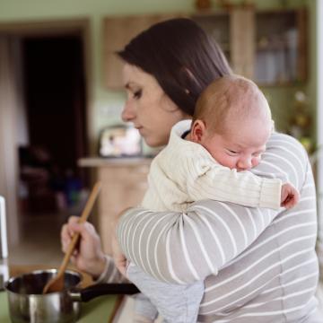 Woman holding a baby while cooking on a stove