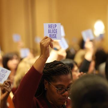 Woman holding a card that says "Help ALICE Rise"