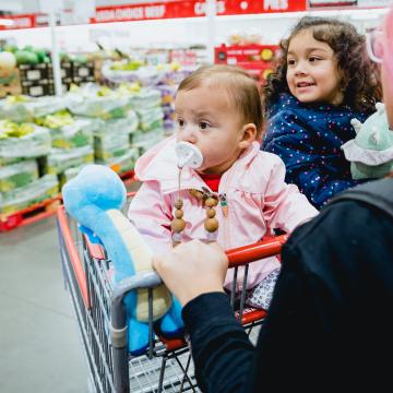 A woman pushing a shopping cart with 2 children in it