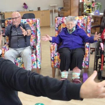 Participants in a chair yoga class open their arms