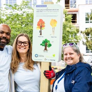 Volunteers smile by Born Learning STEAM Trail sign in Alexandria, Va.