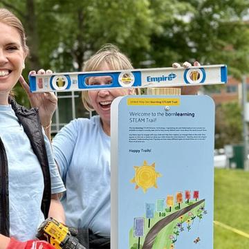 Volunteers from United Way Worldwide and United Way National Capital Area smile holding a level and shovels to install a new Born Learning STEAM Trail in Alexandria, Va.