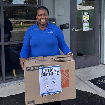 A woman with United Way of Southeast Louisiana holds a box of food donations in front of the New Orleans Resiliency Center