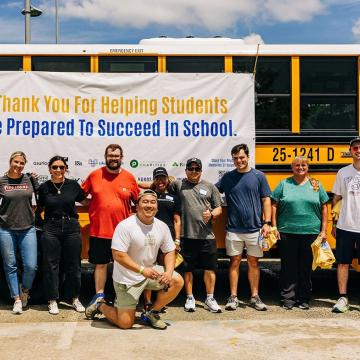 Stuff-the-Bus volunteers with United Way of Greater Nashville pose in front of a school bus at Nissan Stadium