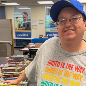 KD Musser, a dedicated volunteer with United Way Rock River Valley in Rockford, IL, stands with her hand on a stack of books